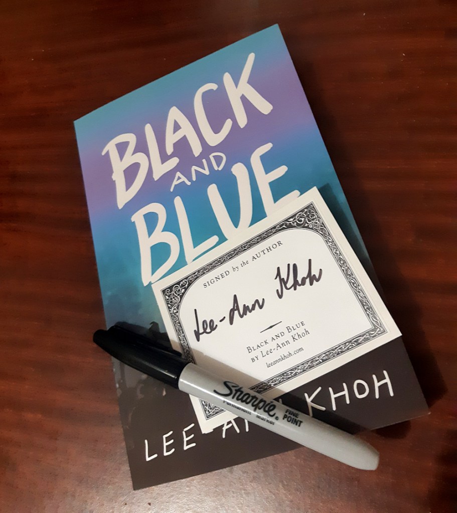A Sharpie marker and a bookplate sticker signed by Lee-Ann Khoh, resting on top of a paperback copy of Lee-Ann's book, Black and Blue.