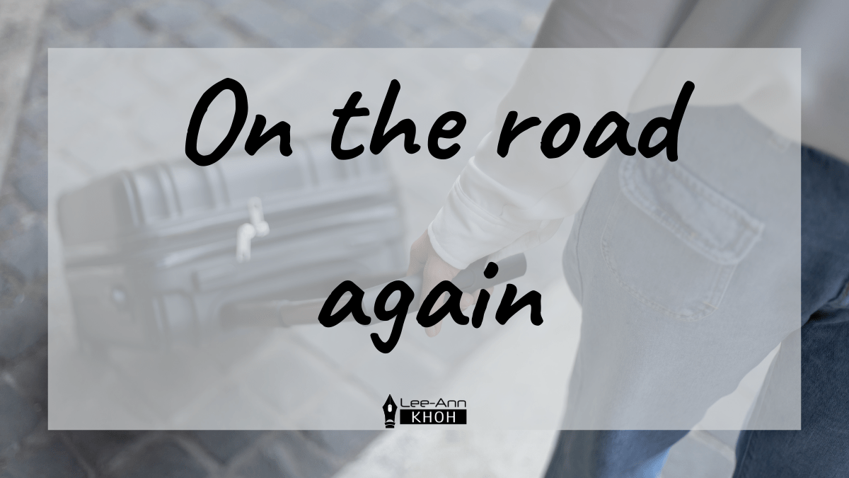 Text reads: On the road again. Background contains someone wheeling a trolley bag.