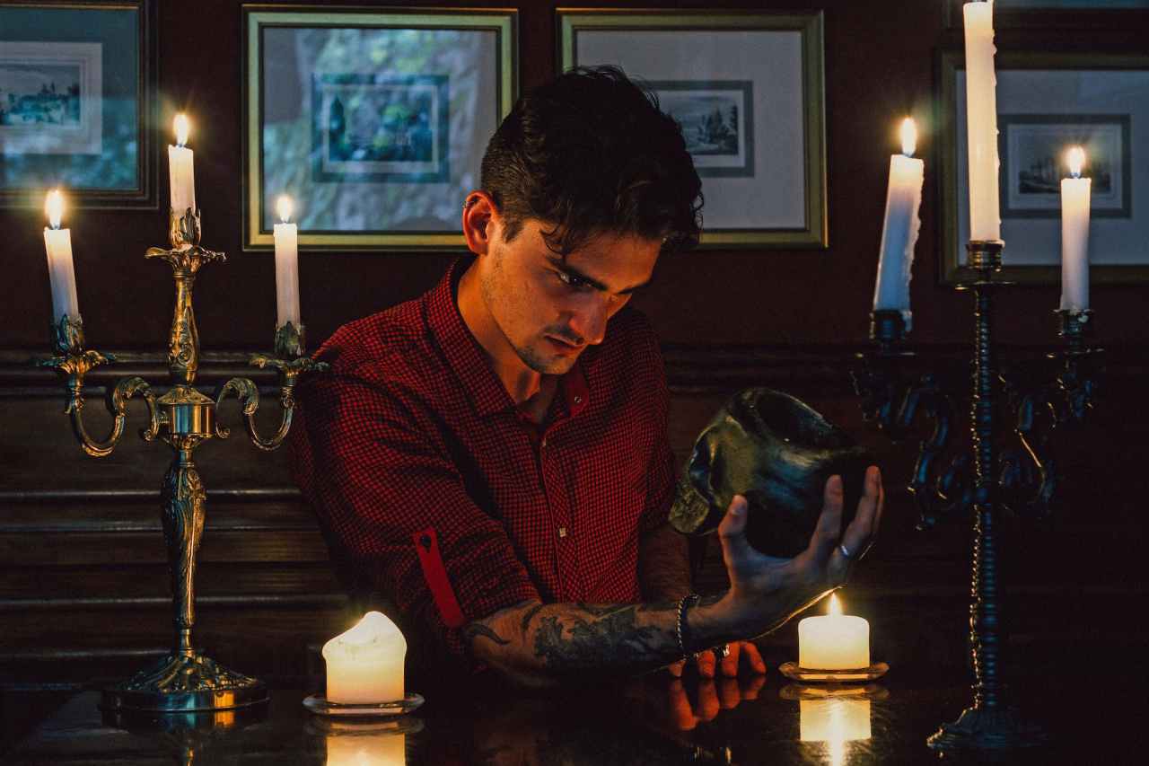 A man holding and staring at a skull, surrounded by candles.
